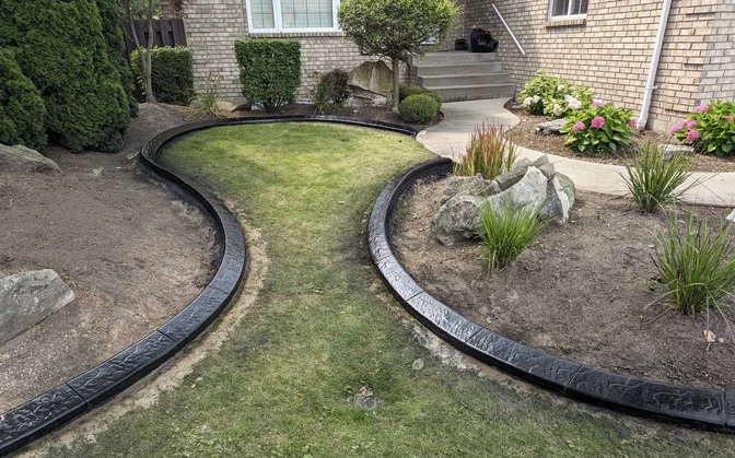 Matte black stamped concrete curb flowing in a long S-curve through a front lawn with rock-garden accents in Windsor Essex County.