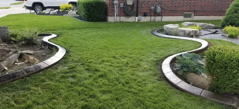 Dark brown stamped concrete curbing edging two garden beds in a lush green backyard lawn at a Windsor Essex County home.